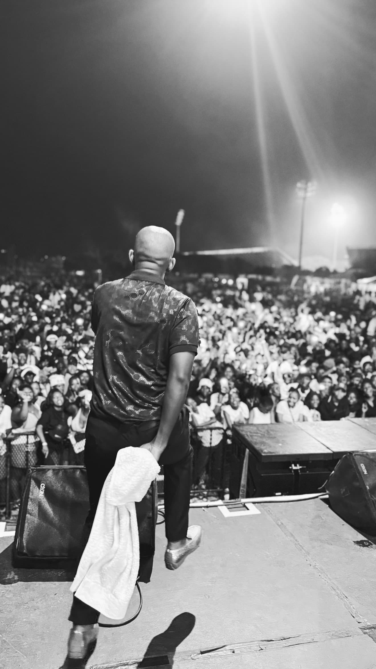 A performer on stage at night, seen from behind, facing a packed festival crowd